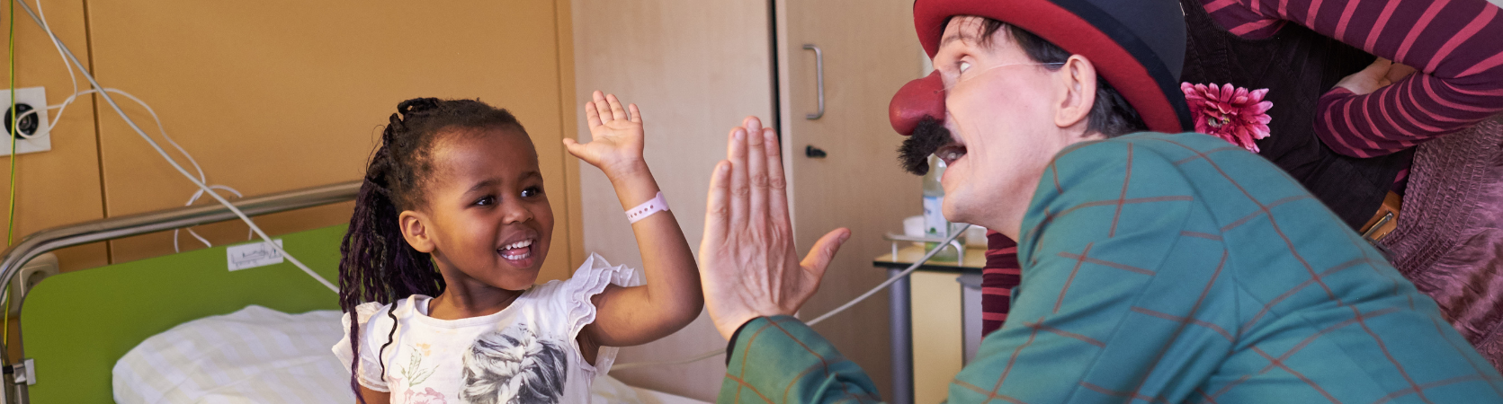 Ein ROTE NASEN-Clown gibt einem kleinen Mädchen im Krankenhaus ein High Five.
